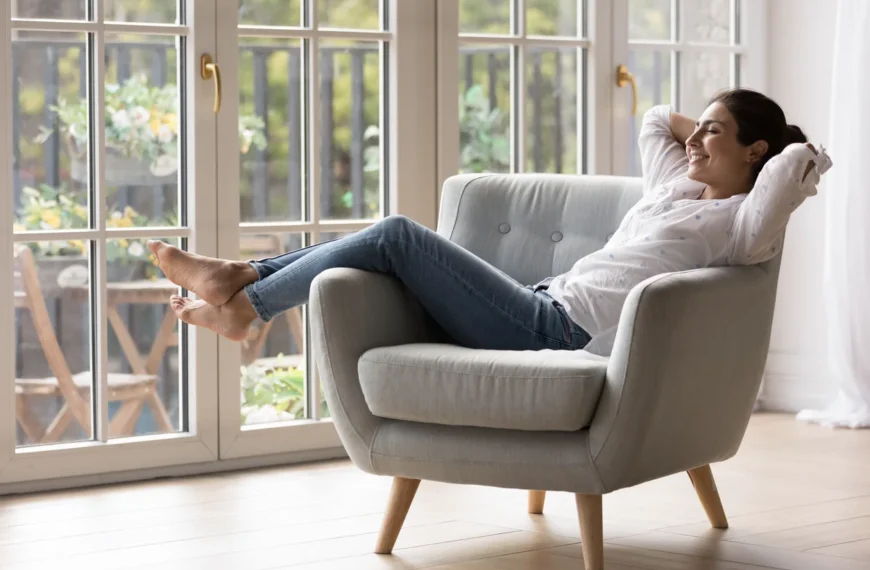 A relaxed woman reclining comfortably in a plush chair, eyes closed with a peaceful smile. Soft natural light fills the serene room, highlighting a calm and healing atmosphere during her recovery session.